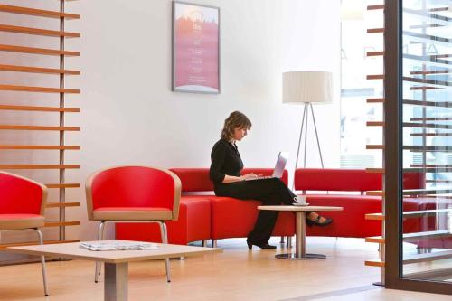 Eine Frau sitzt mit einem Laptop auf einem roten Sofa. in der Unterkunft ibis Delémont in Delémont