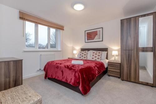 a bedroom with a bed with a red blanket and a window at Royal Apartments - Heathrow in Hillingdon