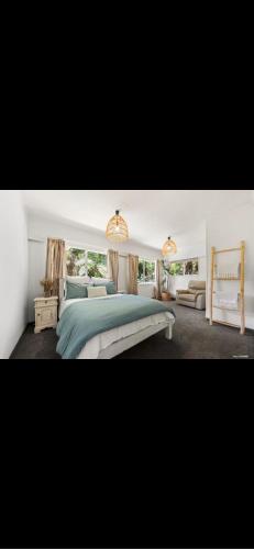 a white bedroom with a bed and a couch at Sunbird House Piha in Piha