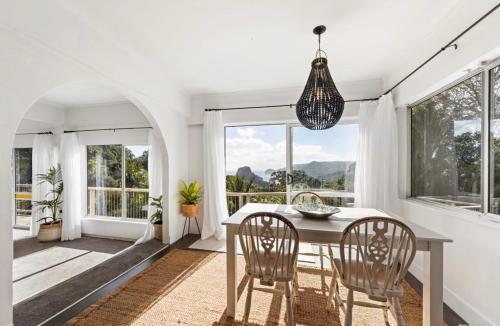 a dining room with a table and chairs and windows at Sunbird House Piha in Piha