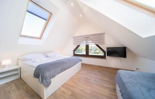 a white attic bedroom with a bed and a tv at Lilu Apartamenty in Dziwnów