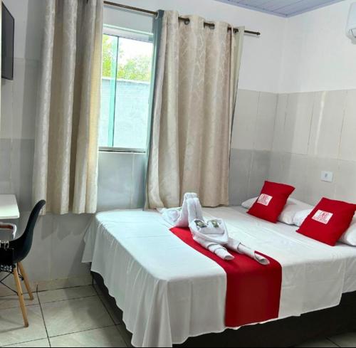 ein Schlafzimmer mit einem Bett mit roten Kissen und einem Fenster in der Unterkunft Alfa Hotel in Nerópolis