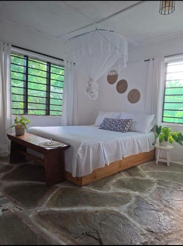 a bedroom with a bed and a table and windows at The Nook,Kilifi in Kilifi