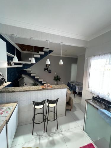 a kitchen with two bar stools and a staircase at Casa com Piscina Privativa e Área Gourmet in Rio das Ostras