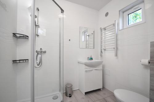 a white bathroom with a shower and a sink at Westbeach House in Grzybowo