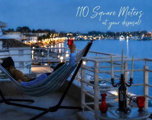 a man laying in a hammock on a balcony overlooking the water at AB Preveza Apartments-15 Meters Over the Sea Attic & Alexander's the Great Executive Suite in Preveza