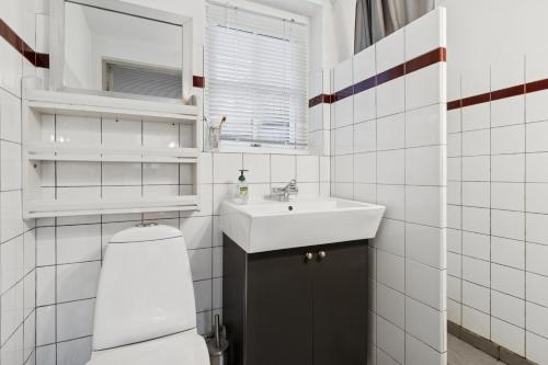 a white tiled bathroom with a sink and a toilet at Family-Friendly Beachside Holiday Home in Rønne