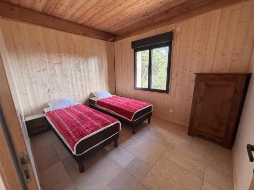 two beds in a room with wooden walls and a window at L'ecorce sauvage 4/6 pers in Rocles