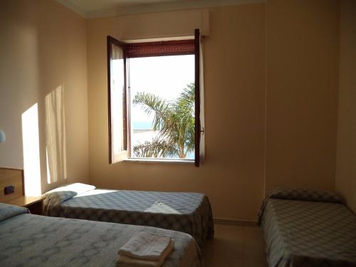 a room with two beds and a window with a palm tree at Villaggio Club Tortorella in Marina di Casalvelino