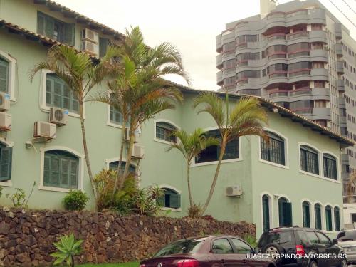 a white building with palm trees in front of a tall building at Pousada Recanto da Prainha in Torres