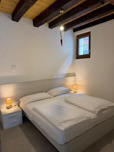 a bedroom with a white bed with two lamps and a window at Cozy tiny flat in Cadore Dolomiti in Calalzo