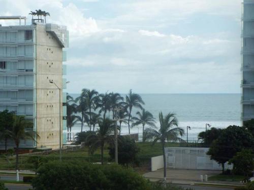 a tall building next to the ocean with palm trees at Puerta diamante acapulco in Acapulco