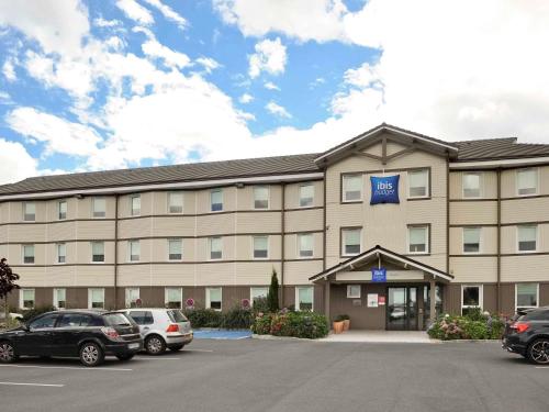 a hotel with cars parked in a parking lot at Ibis Budget Bayeux in Bayeux