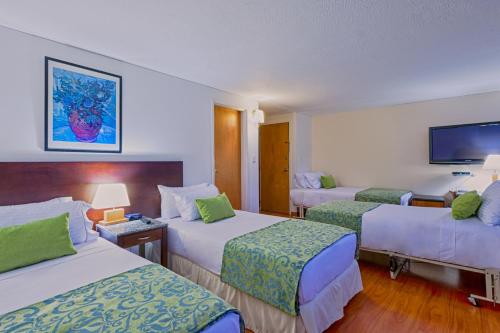 a hotel room with three beds and a tv at Hotel Oceanía Bogotá Museo in Bogotá