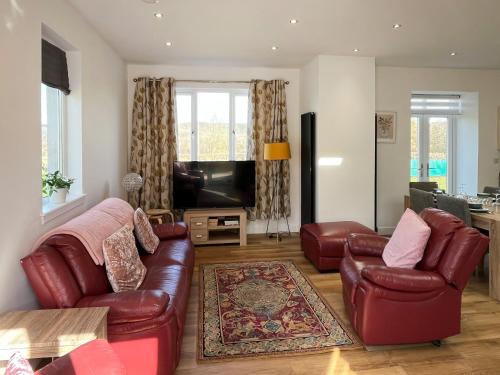 a living room with red leather furniture and a flat screen tv at North Lodge in Forgandenny