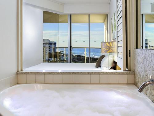 a bath tub in a room with a large window at The Sebel Maroochydore in Maroochydore