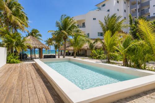 a pool at the beach with palm trees and a building at Arenika Beachfront Villa & Rooms in Puerto Morelos