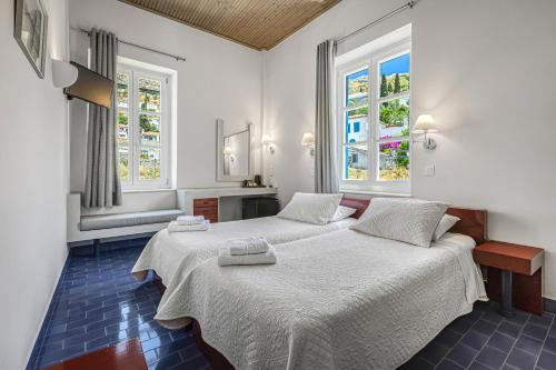 two beds in a room with two windows at Greco Hotel in Hydra