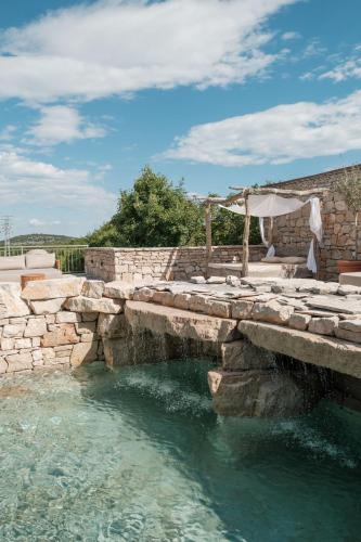 a pool with a stone wall and an umbrella at Nono Ban Boutique Hotel & Villas in Gornji Humac