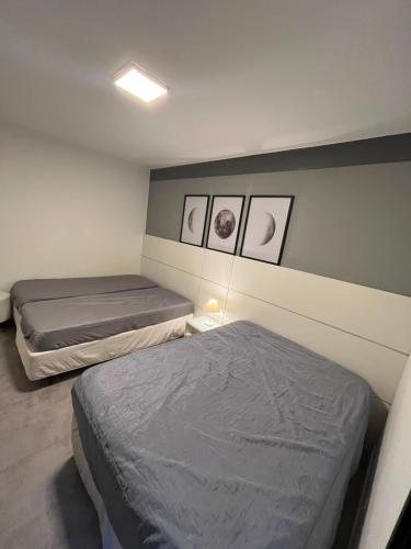 two beds in a room with three pictures on the wall at Apto Riviera Piscina Aquecida in Bertioga