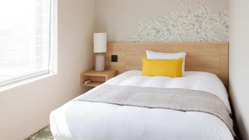 a bedroom with a white bed with a yellow pillow at Hotel Terrace the Garden Mito in Mito