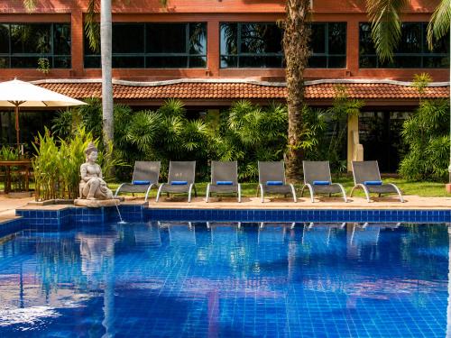 a swimming pool with chairs and a statue in front of a building at Nova Park Hotel Pattaya in Pattaya