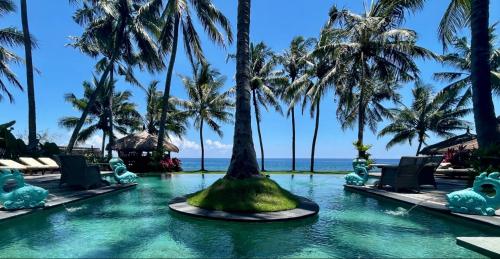 a pool at the resort with palm trees and the ocean at Louka Beach Bali in Tianyar