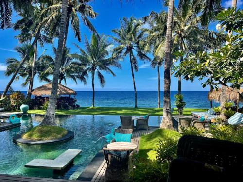 a resort pool with palm trees and the ocean at Louka Beach Bali in Tianyar