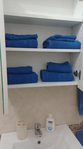 a bathroom with blue towels on shelves with a sink at Perla del mare Ionio in Fondachello