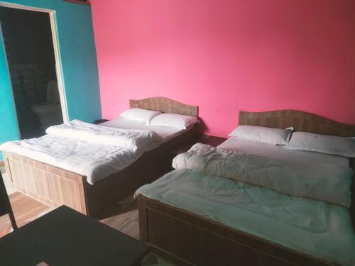 two beds in a room with a pink wall at Hotel crunchy shadowbegnas in Deorāli
