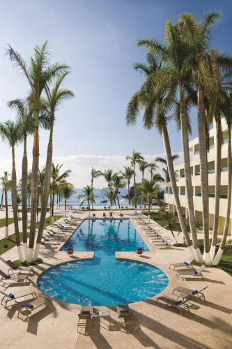 a pool with chairs and palm trees and a building at Dreams Huatulco Resort & Spa in Santa Cruz Huatulco