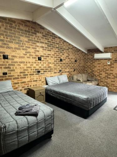 a bedroom with two beds and a brick wall at Clock Tower Motor Inn in Coonabarabran