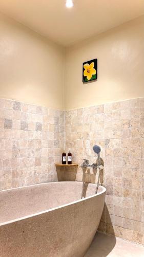 a large tub in a bathroom with a flower on the wall at Kuda Putih Guest House Pandawa in Ungasan