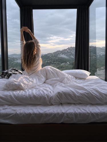 a woman laying in bed looking out of a window at Lazord Glass Bungalow Trabzon in Geçit