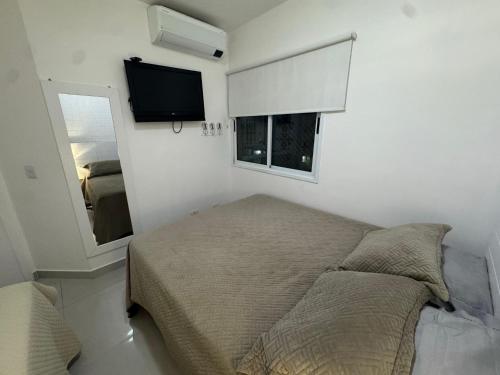 a bedroom with a bed and a window and a television at Flat lindo a 120 metros da praia de Riviera de São Lourenço até 4 pessoas in Bertioga
