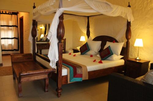 a bedroom with a canopy bed with a chair and a table at Zawadi Beach Villas in Matemwe