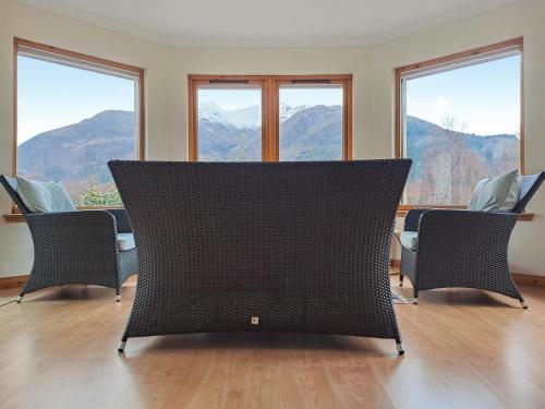 a room with chairs and windows with mountains in the background at Nether Carness in North Ballachulish