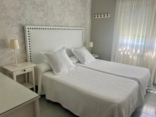 a white bedroom with a bed with white sheets and pillows at Viviendas Uso Turístico Arzúa in Arzúa