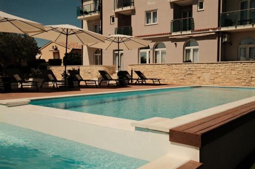 a swimming pool with chairs and umbrellas next to a building at Villa Mirko in Barbariga