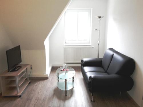 a living room with a black leather couch and a glass table at Pension Marktblick in Friedrichstadt