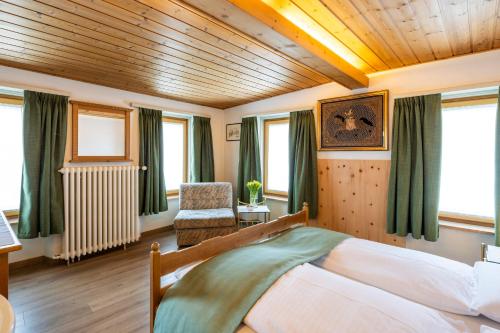 a bedroom with a bed and a chair and windows at Hotel Alpina in Zernez