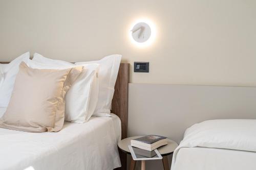 two beds with white pillows and a table with a book at Hotel Estense in Gatteo a Mare