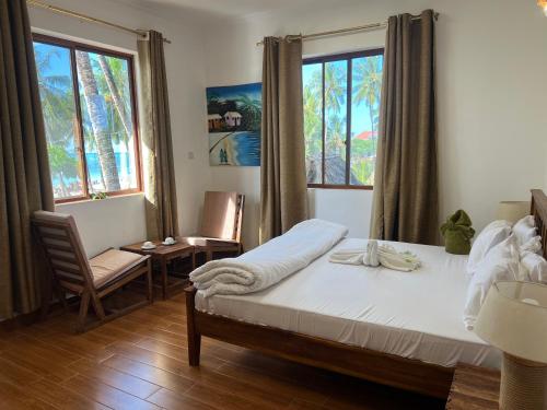 a bedroom with a bed and a chair and two windows at Aurora Nungwi in Nungwi