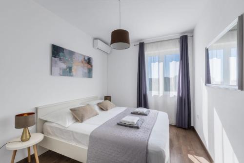 a white bedroom with a bed and a window at Maslina in Vrsi