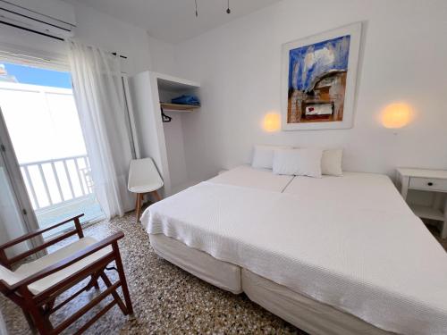 a white bedroom with a bed and a chair at Windmill Rooms in Antiparos