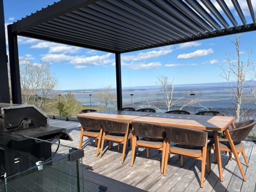 a wooden table and chairs on a deck with a grill at Le Föss, Fleuve, Sauna & Spa in Petite-Rivière-Saint-François