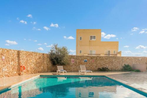 a swimming pool with two chairs and a building at Wellness Hygge Modern Gozitan Apartment - Happy Rentals in Taʼ Sardina