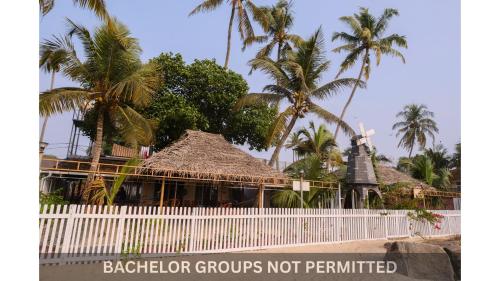 a building with a white fence and palm trees at Jonirene Seasands Homestay in Alleppey