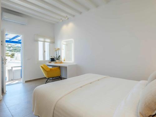 a white bedroom with a bed and a yellow chair at Plateia House Mykonos in Mikonos