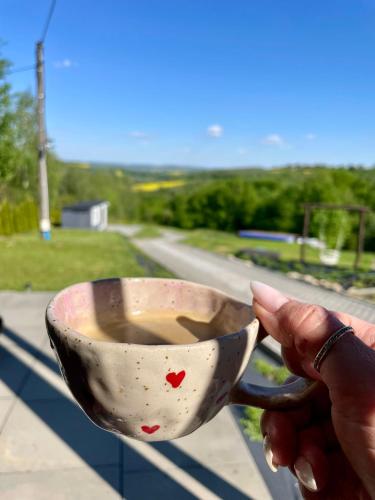 a person holding a cup of coffee on a balcony at Domek Na Wzgórzu Roztocze in Majdan Abramowski